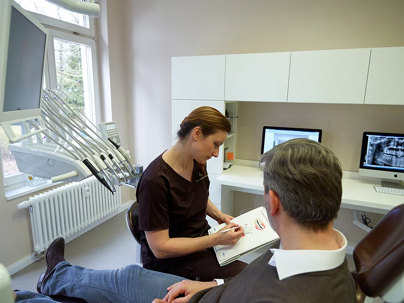 Einem Patienten wird etwas von der Zahnärztin erklärt.
