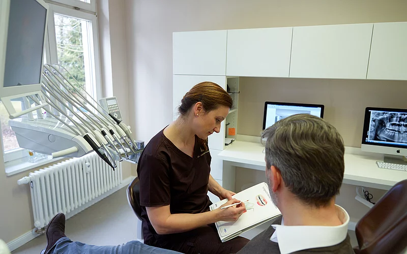 Einem Patienten wird etwas von der Zahnärztin erklärt.