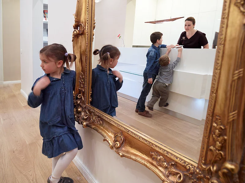 Die Zahnärztin schaut über der Theke. Dahinter stehen drei Kinder.