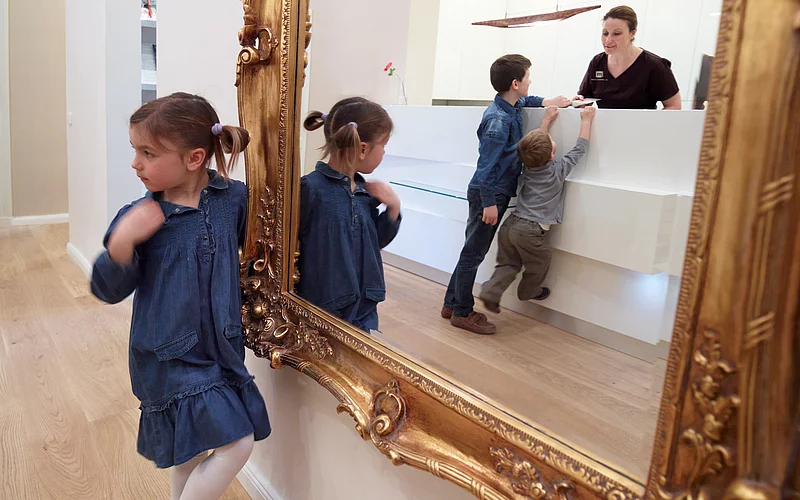 Die Zahnärztin schaut über der Theke. Dahinter stehen drei Kinder.